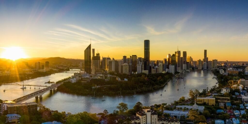 A wide brown river edged with mangroves and leafy riverside homes at sunrise